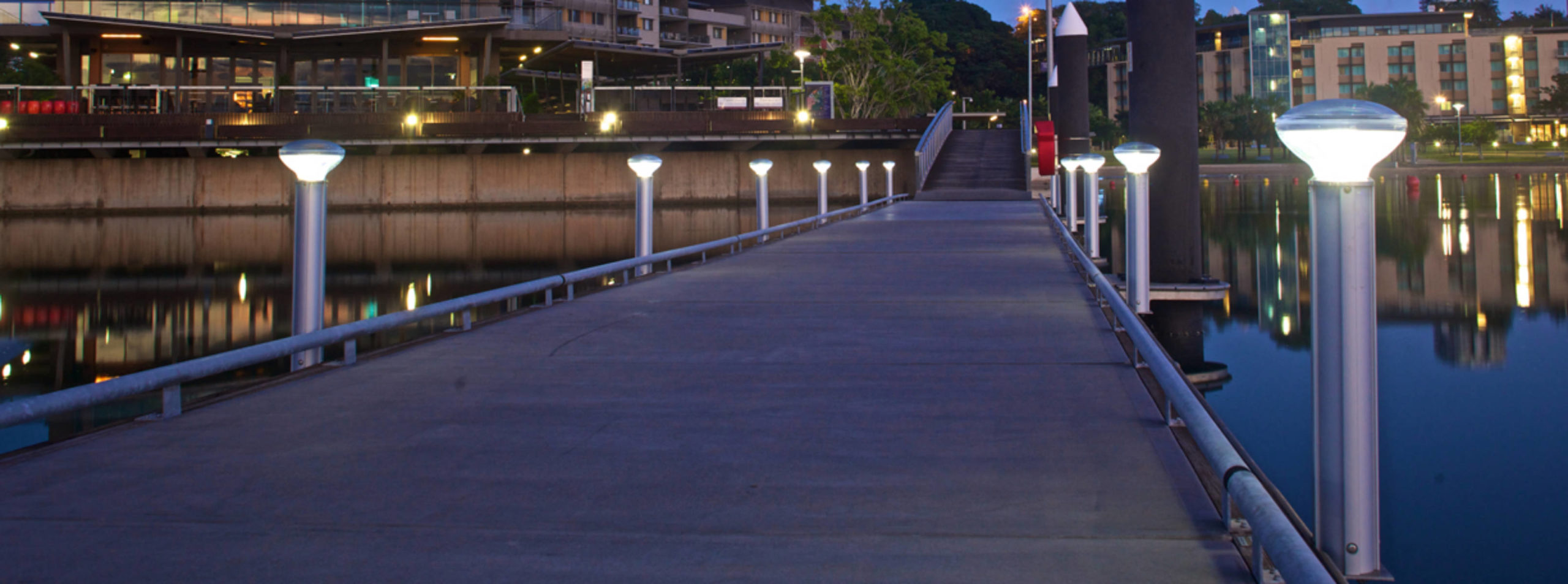 Illuminated solar bollards along a marine jetty and pontoon walkway at blue hour